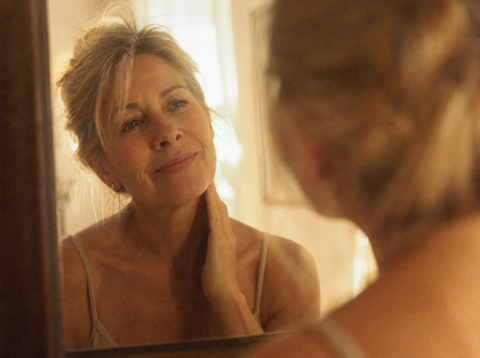 A woman looking at her reflection in a bathroom mirror in morning light